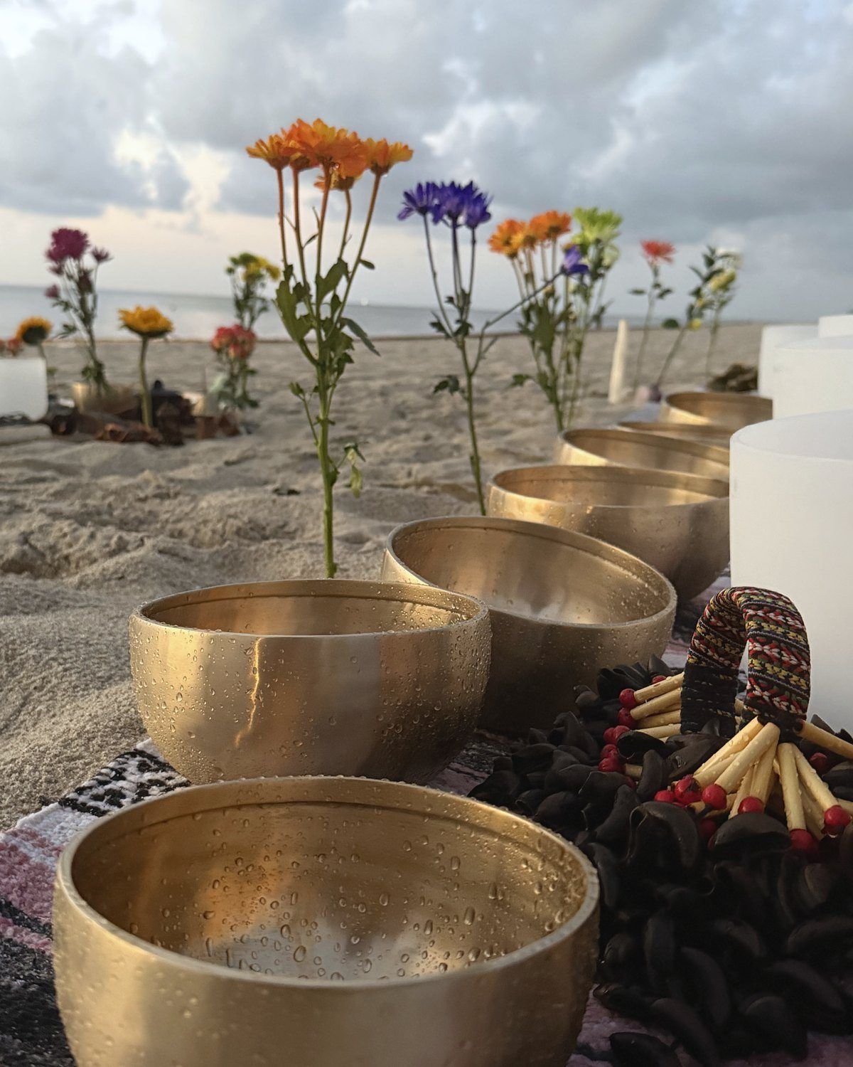 Bowls and a crystal bowl on the sand, the sea and a cloudy sunrise behind