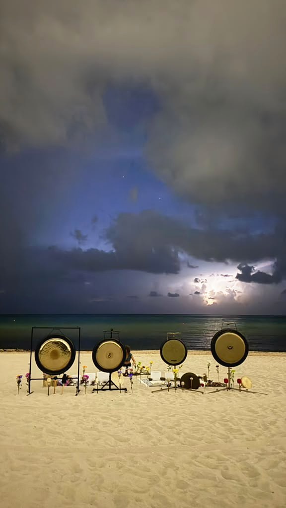 Four gongs set in the sand at the shoreline under a storm sky, lightning over the sea